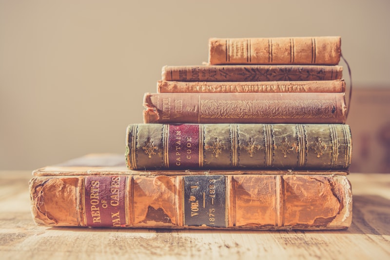 A thick open book with dense text on a desk lit by a lamp