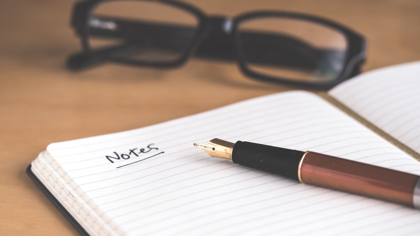 A hand writing notes in a notebook beside an open book on a desk