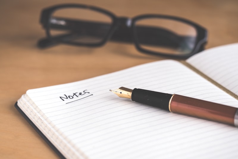 A hand writing notes in a notebook beside an open book on a desk